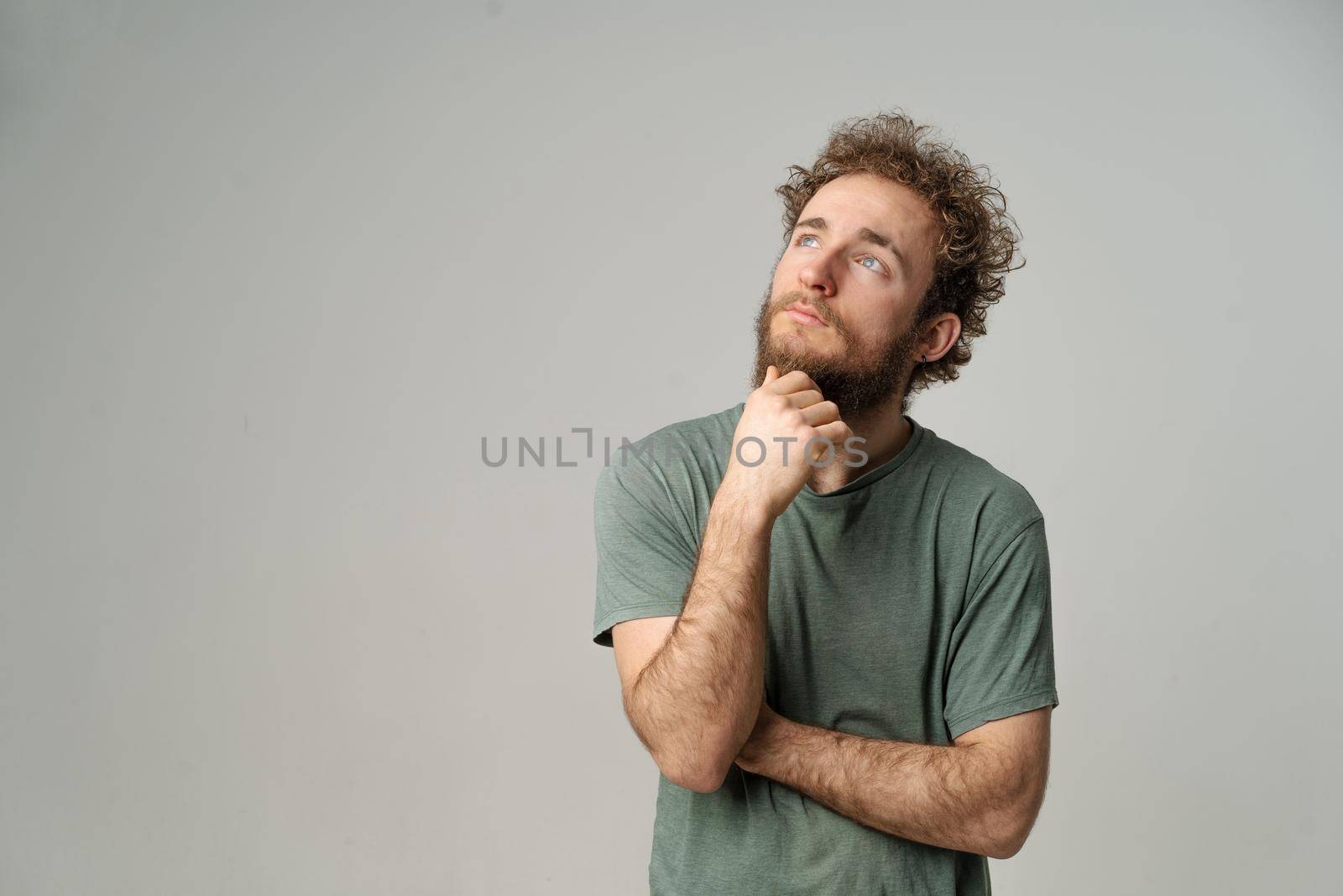 Dreamy Curly Guy Looks to the Copy Space ,Thoughtful Man Thinks about his Future. Male Model in Graphite T-shirt Posing in Studio with Light Gray Background. Close-up. High quality photo