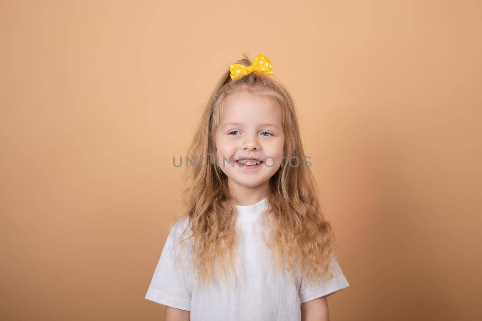 portrait of a sweet blonde little girl in white t-shirt and with yellow bow on her head. on brown background.