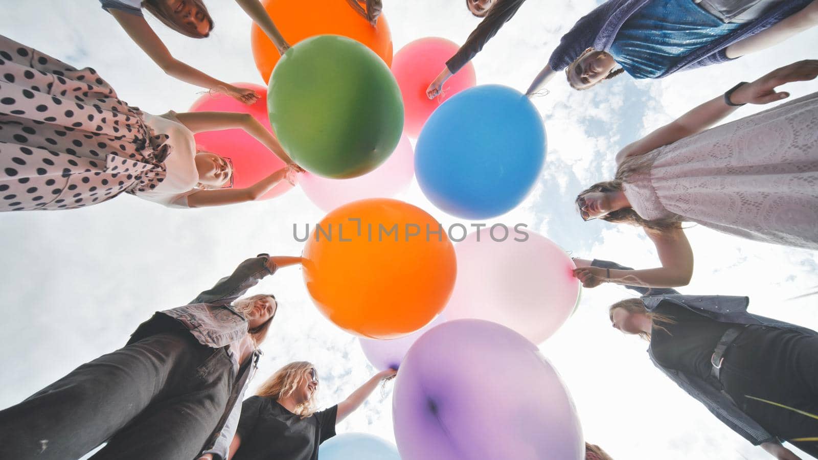 Cheerful girlfriends connect large colorful balls in a circle. by DovidPro