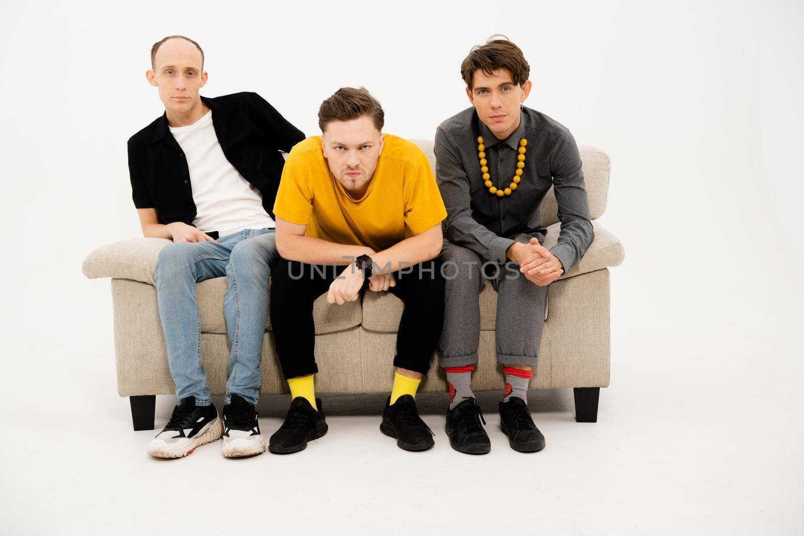 Friends concept. Young Guys Sit on a Sofa on a White Background and Look Together at the Camera. Three Friends are Sitting on the Couch and Watching TV, Watching a Home Theater Together. Close-up. High quality photo