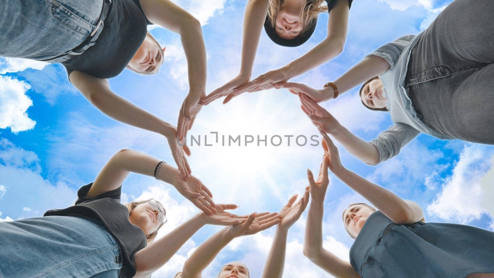 Friends make a circle with their palms against the blue sky