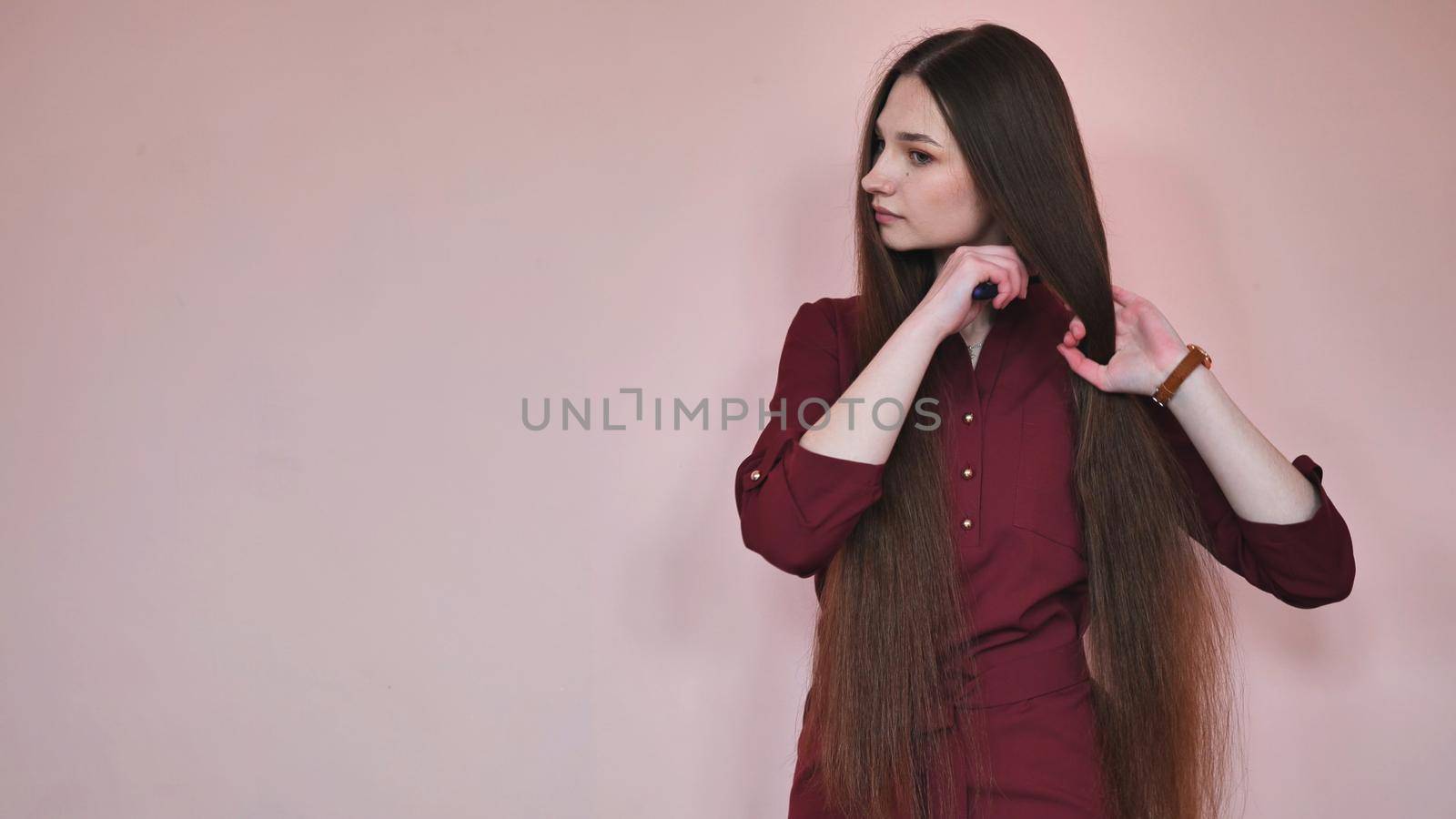 Long-haired girl combs her hair on a pink background