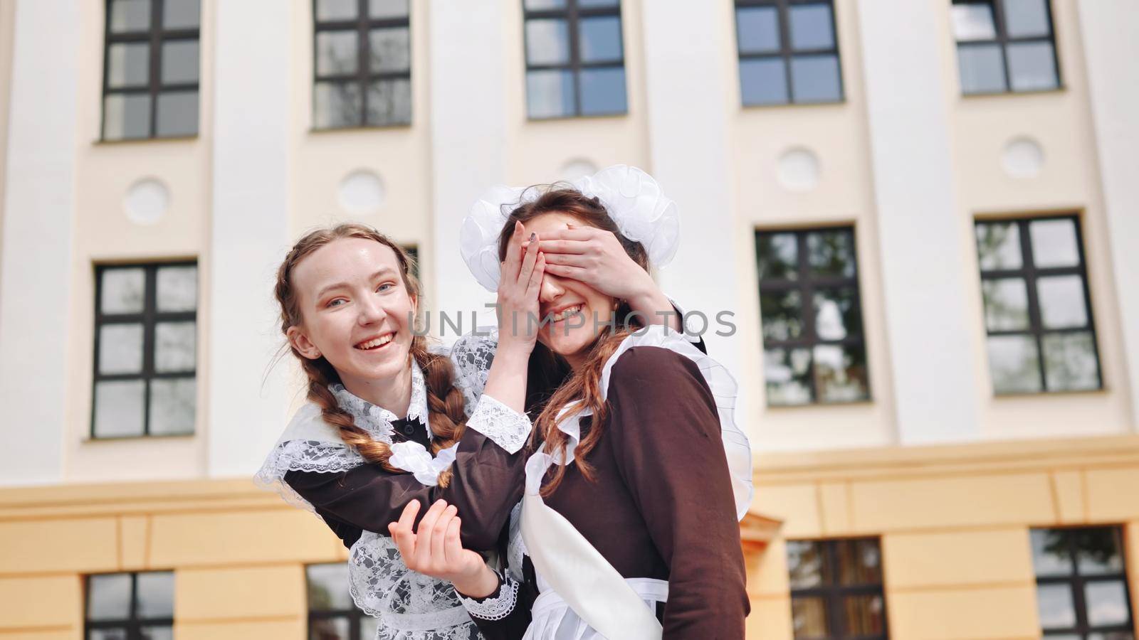 Happy schoolgirl graduate closes her friend's eyes. by DovidPro