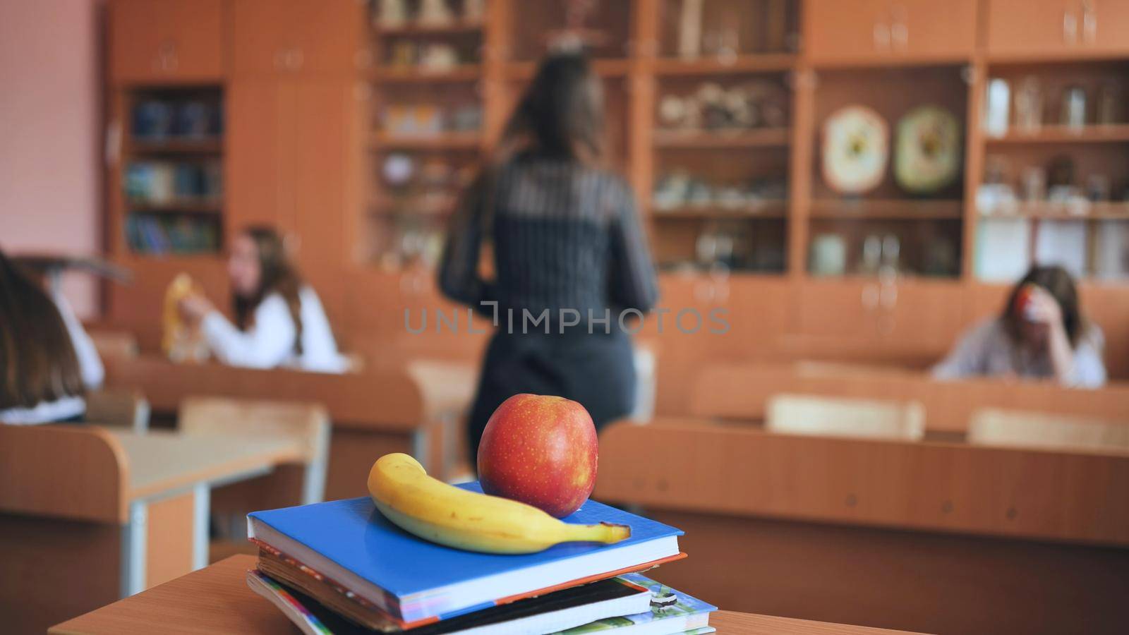 An apple and a banana lie on the books in an empty classroom between lessons