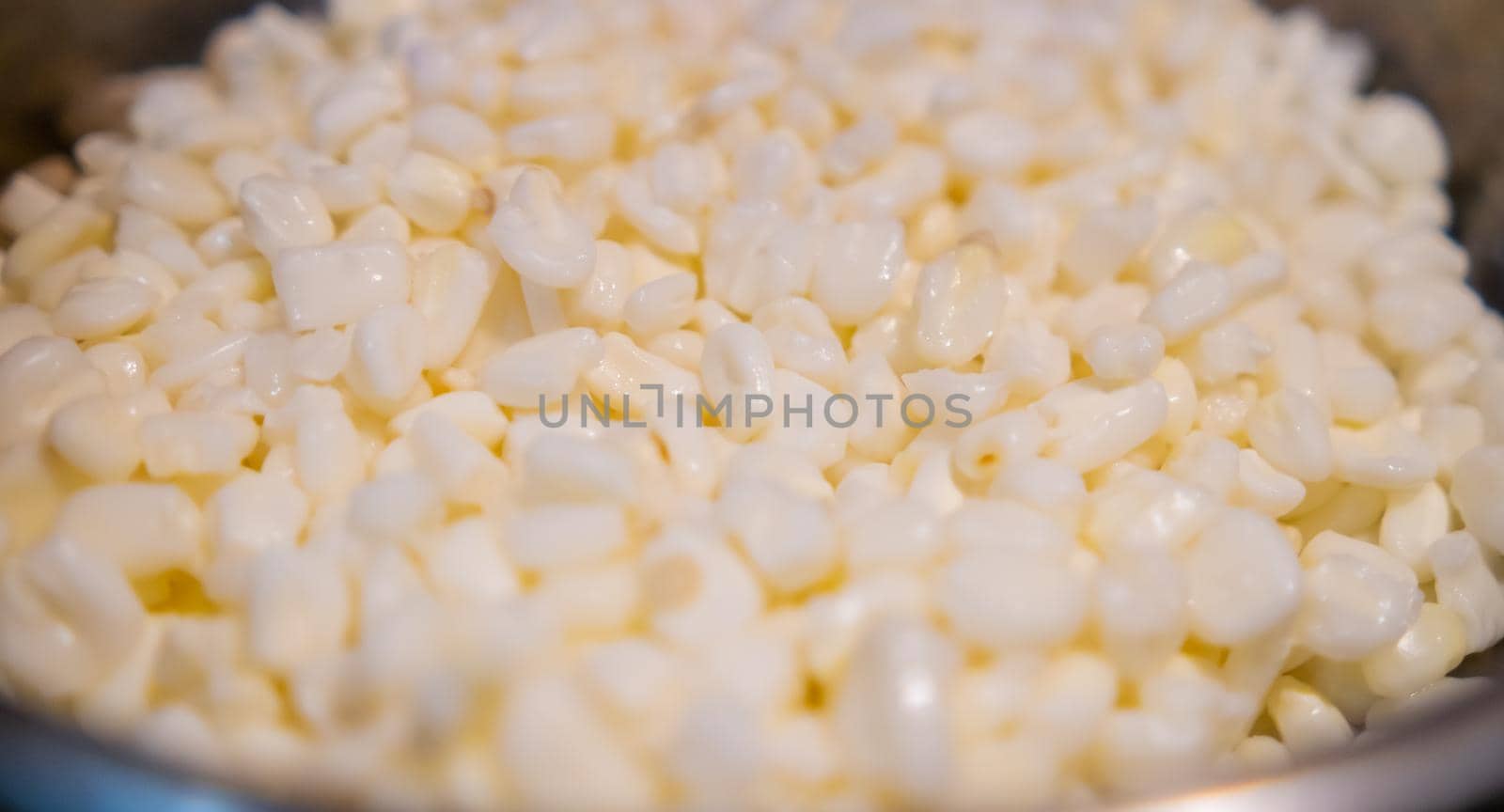 Close-up of pile of uncooked white corn kernels in cooking pot. Several fresh raw corn grains in pot. Authentic meal preparation