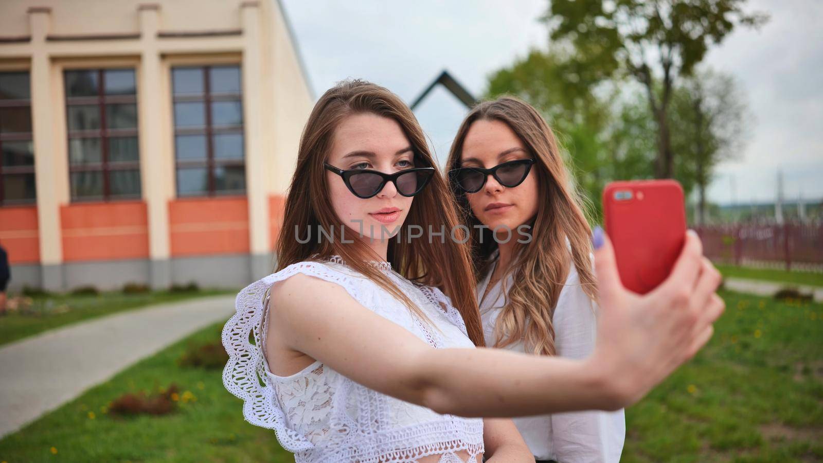 Two girls schoolgirls make a selfie using a smartphone against the background of the school