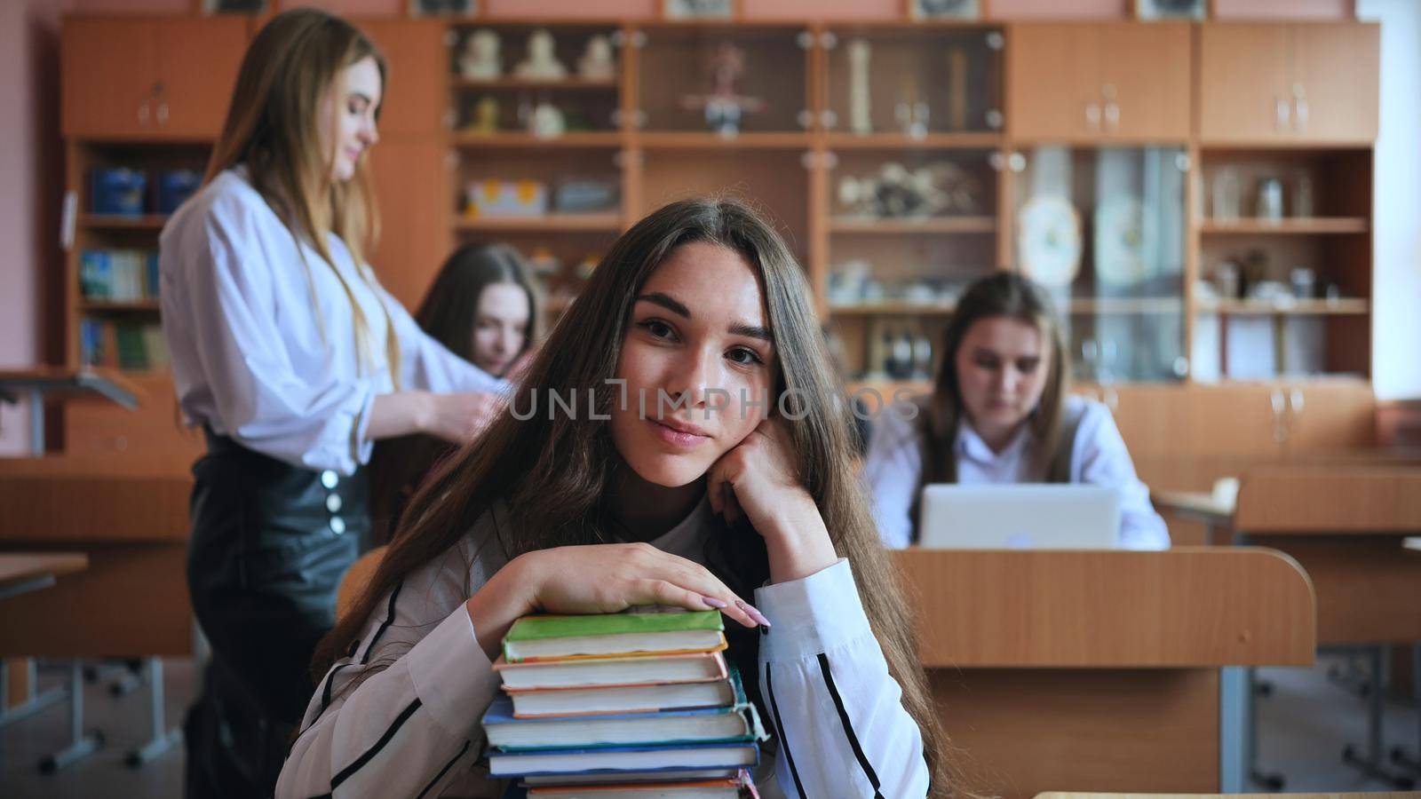 A student poses with textbooks at her desk in her class. by DovidPro