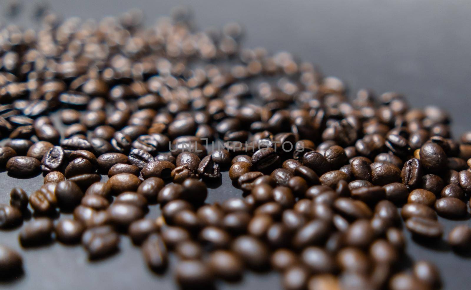 Close-up of small pile of roasted coffee beans with dark gray background. Group of coffee grains scattered on dark color surface. Caffeine and drink preparation