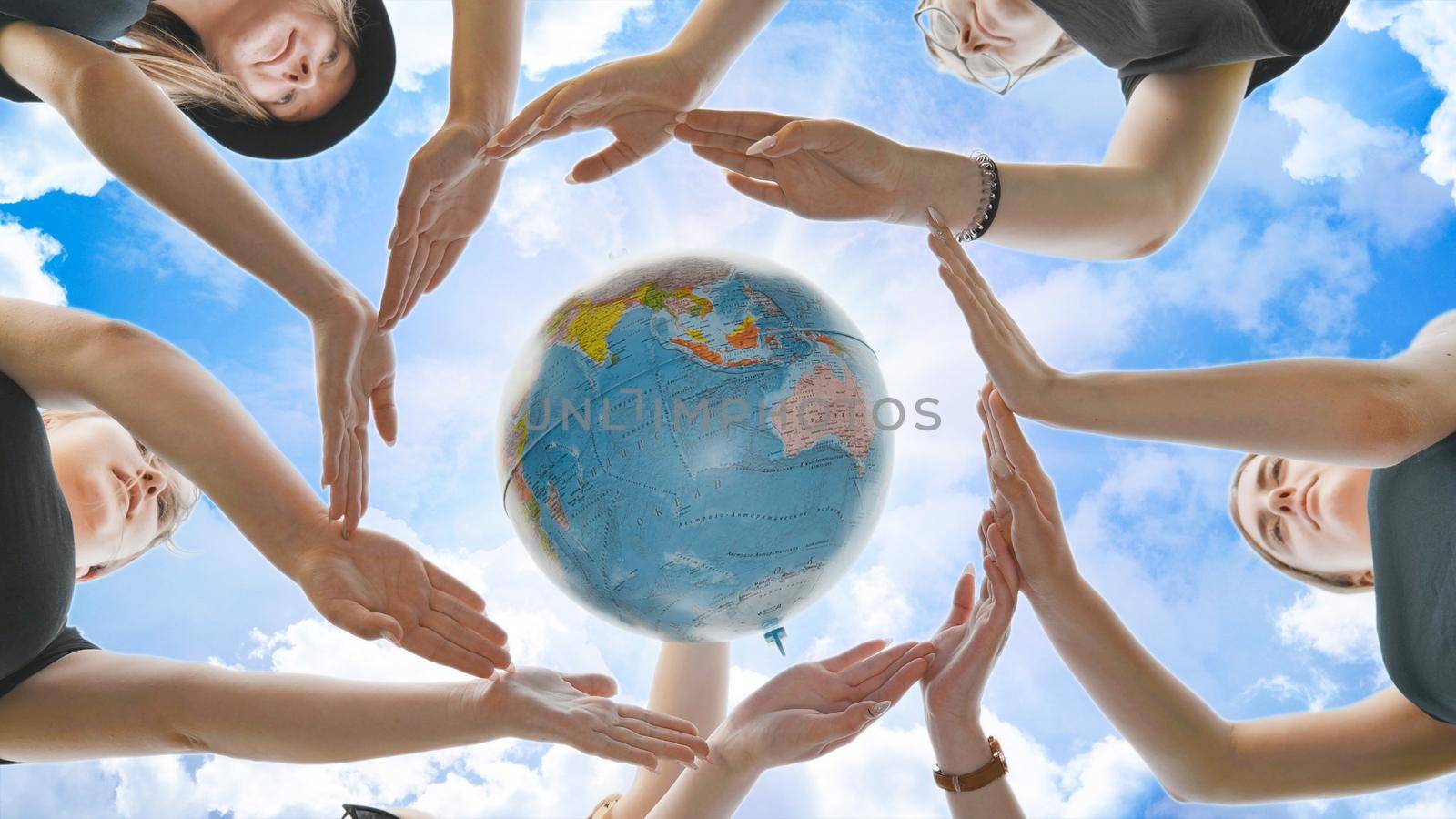 Schoolgirls hug the earth globe with their hands, making a circle out of them on the background of the magic sky