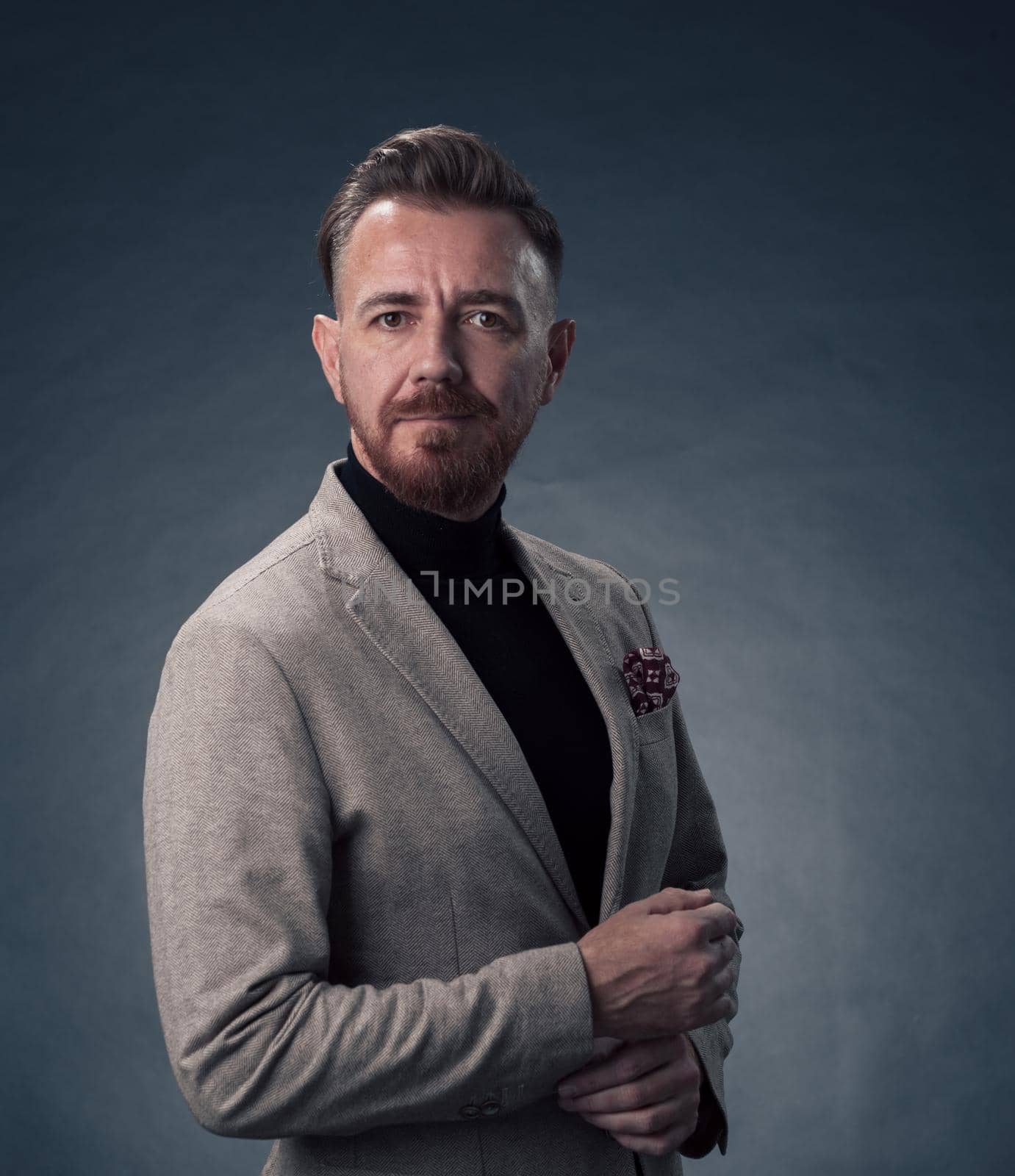 Portrait of a stylish elegant senior businessman with a beard and casual business clothes in photo studio isolated on dark background gesturing with hands. High quality photo