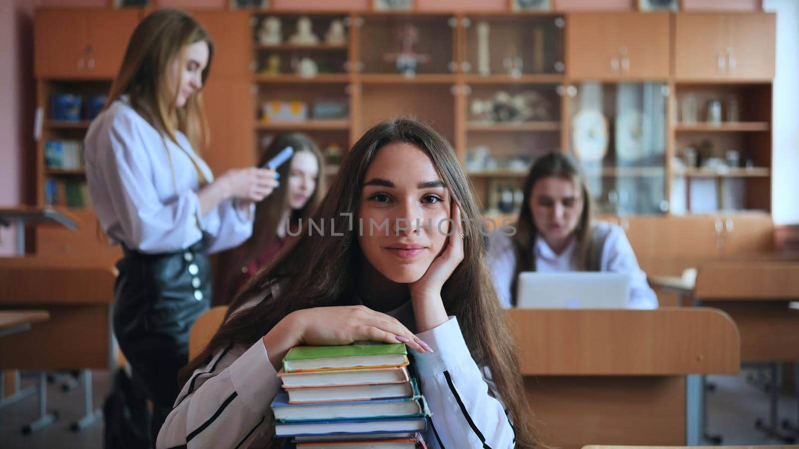 A student poses with textbooks at her desk in her class. by DovidPro