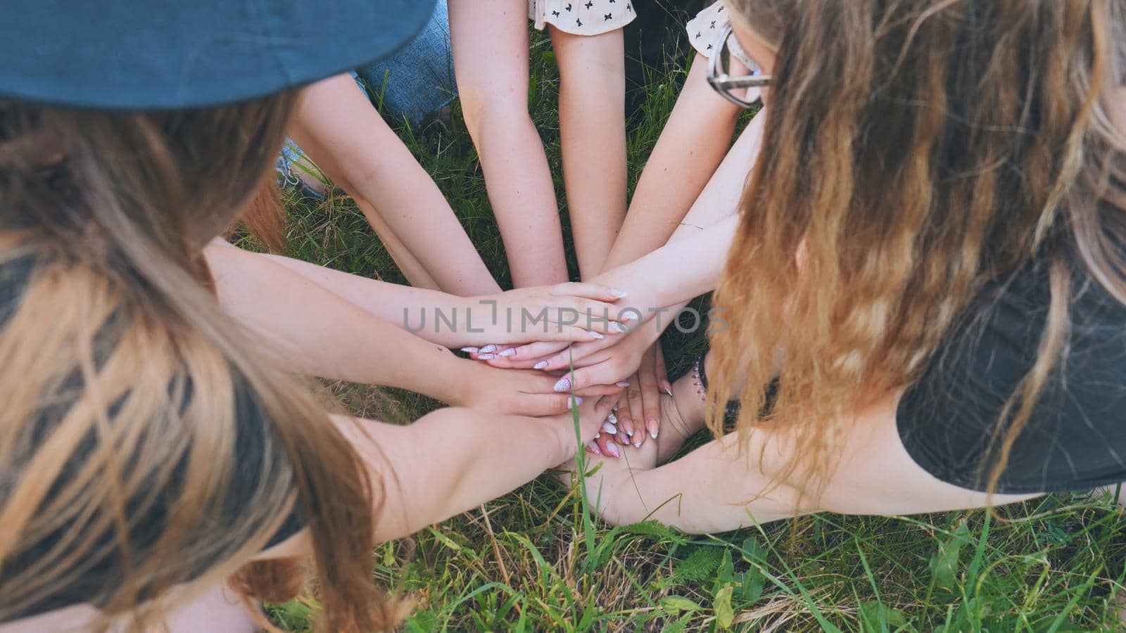 Girls friends join hands on the grass in the park. by DovidPro