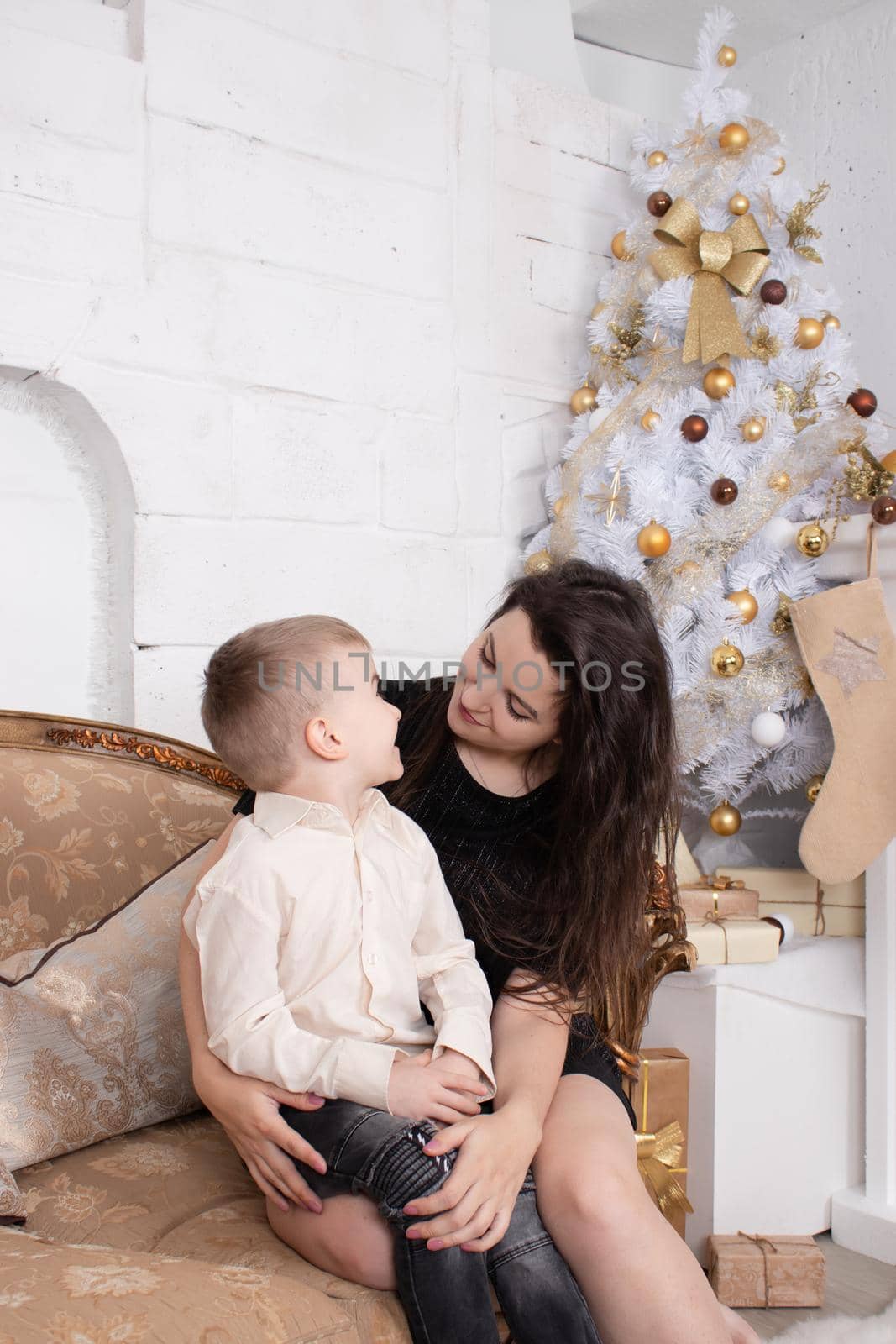 Atmosphere of coming holidays. portrait of happy single mother with her little pleasant boy in white bright room near christmas tree in golden tones by oliavesna