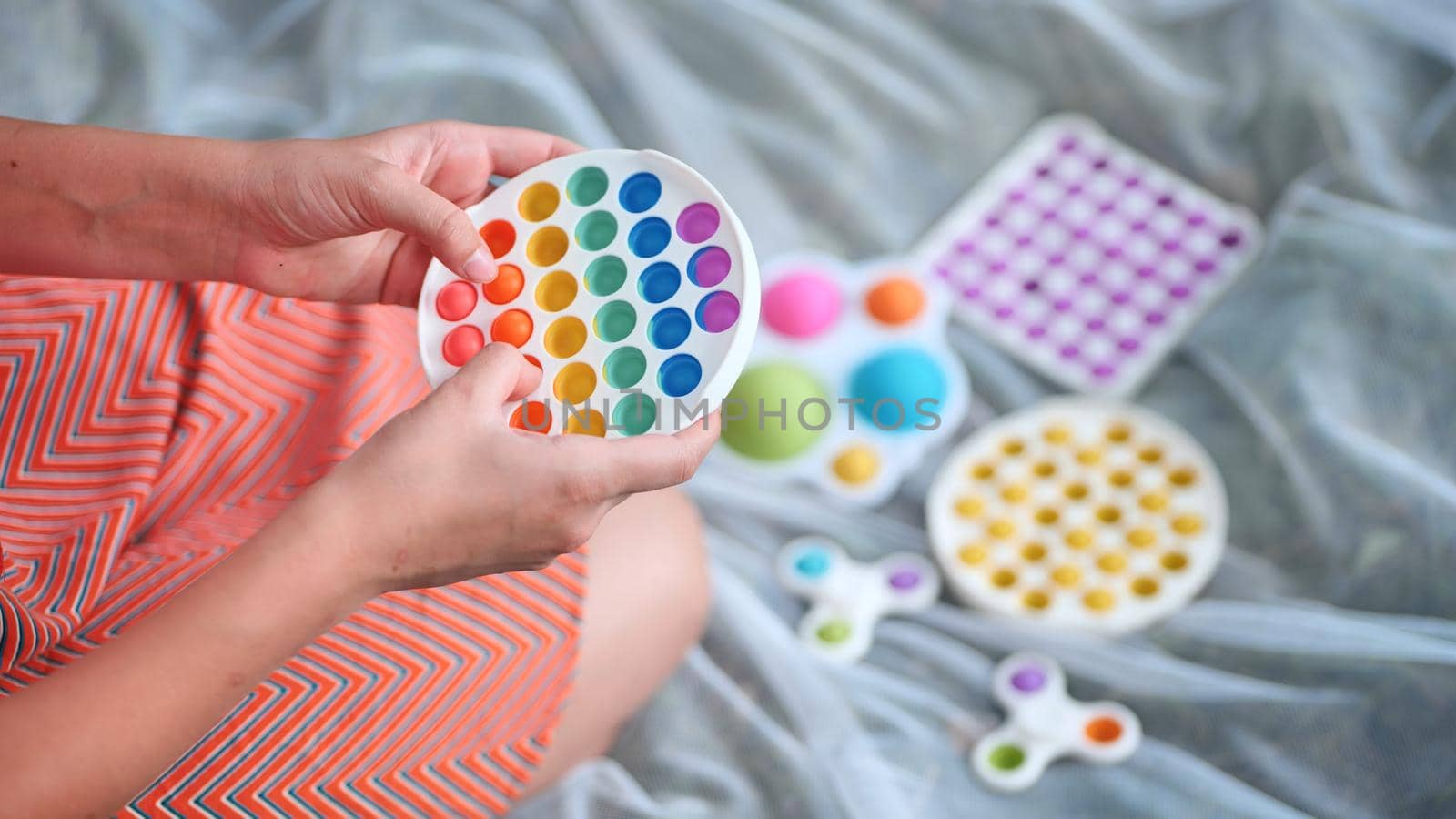 Teen girl plays with anti-stress multicolored toys popit and simple dimple in the park on a summer day