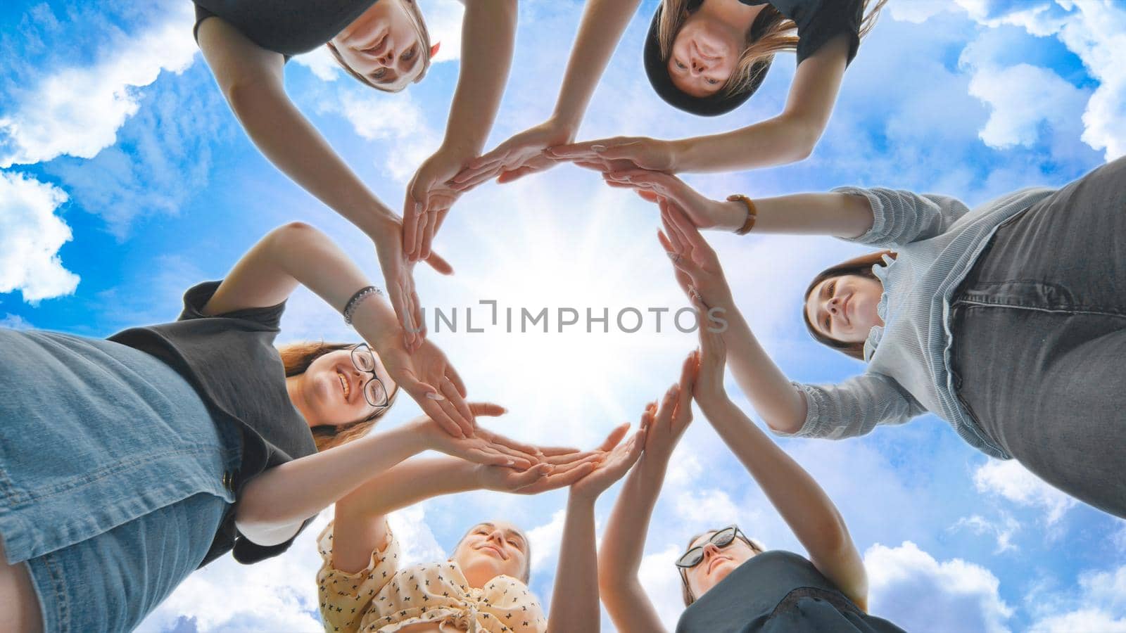 Friends make a circle with their palms against the blue sky