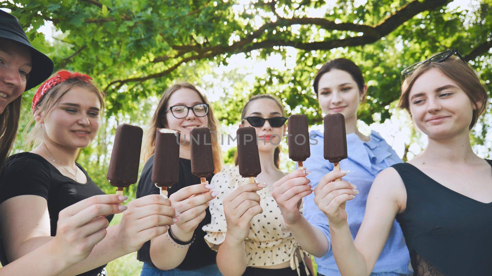 Girlfriends hold chocolate ice cream on a stick in a row