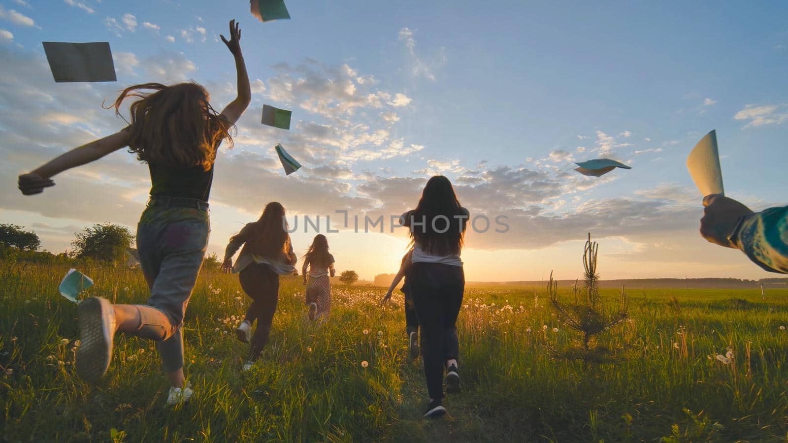 Cheerful students run throwing notebooks after school at sunset