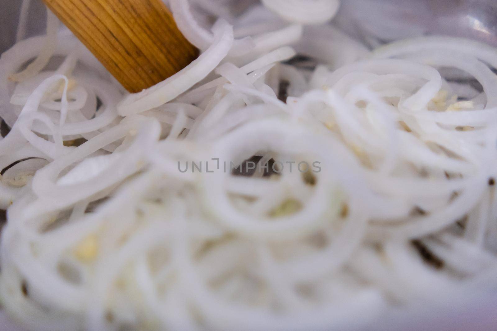 Extreme close-up of wooden spoon on group of onion slices in metal pot. Cooking fresh pile of sliced white vegetable in pot. Healthy meal preparation