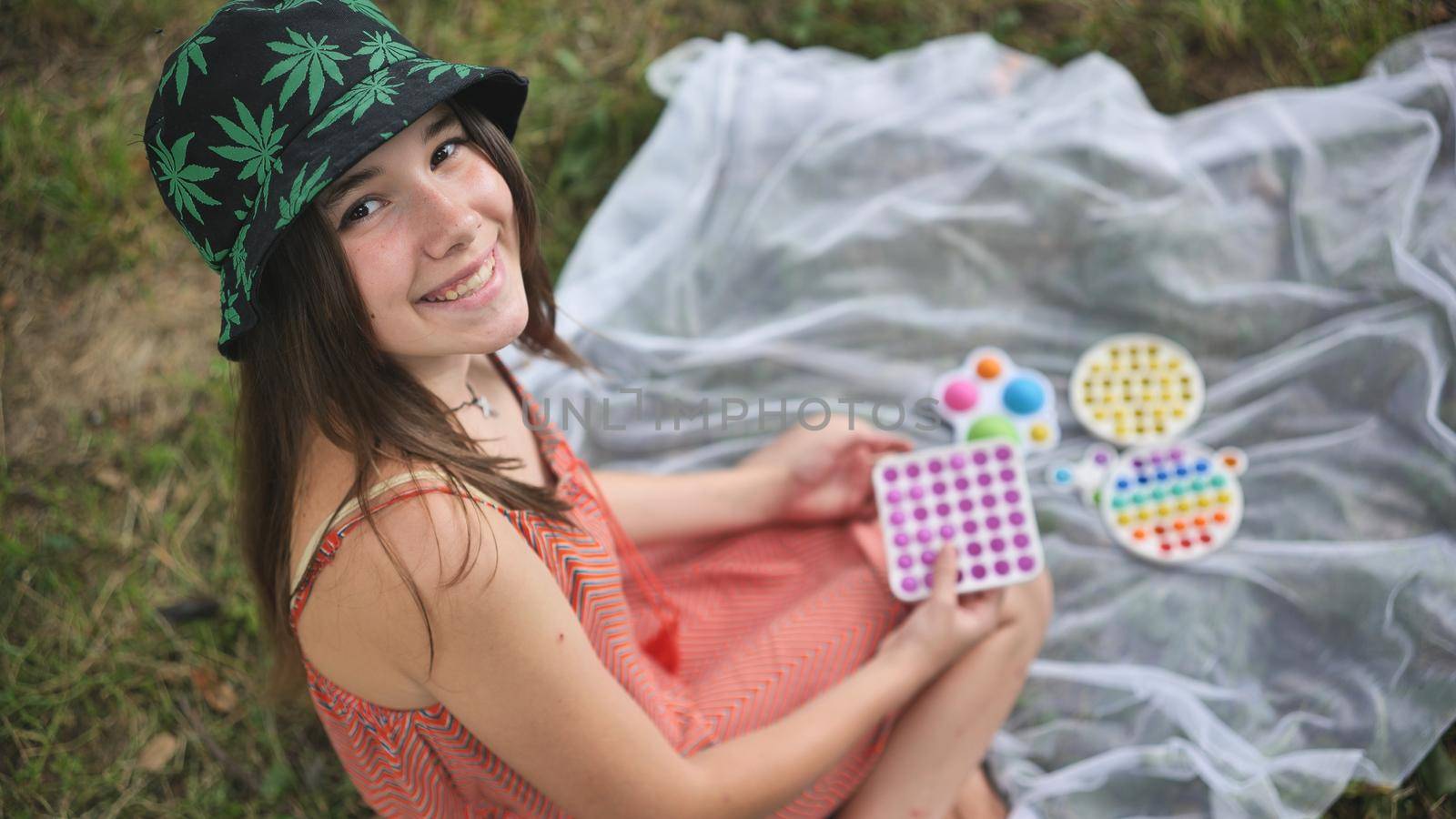 Smiling girl plays with anti-stress toys popit and simple dimple in the park on a summer day. by DovidPro