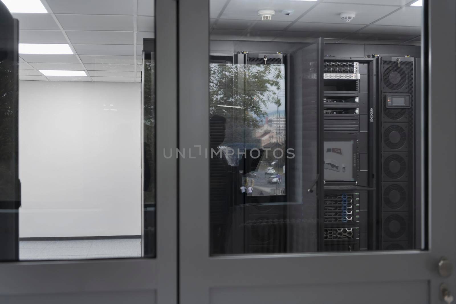 Software Engineer Working on a Laptop Computer in a Modern Server room. Monitoring Room Big Data Scientist in reflection of the entrance door. High quality photo
