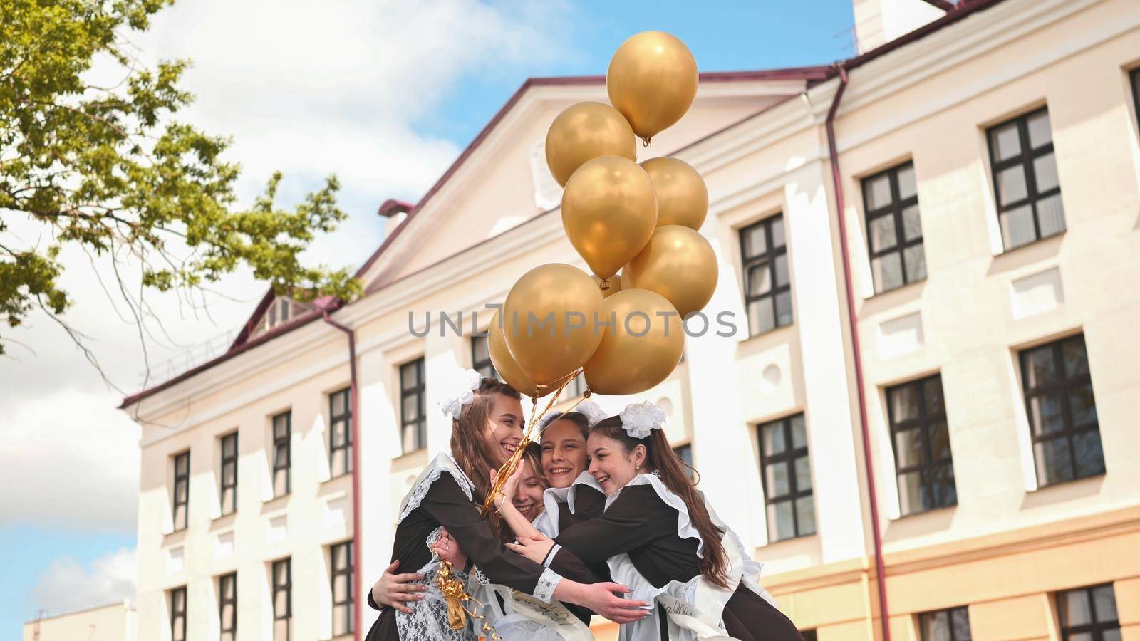 Cheerful Russian girls graduating with orange balloons on the last school day. by DovidPro