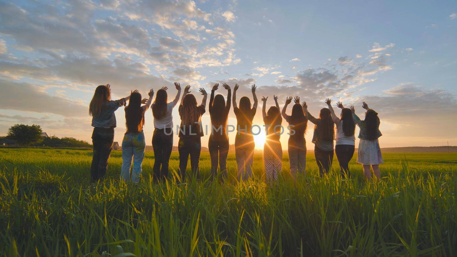 Silhouette of friends of 11 girls waving their hands at sunset in the field