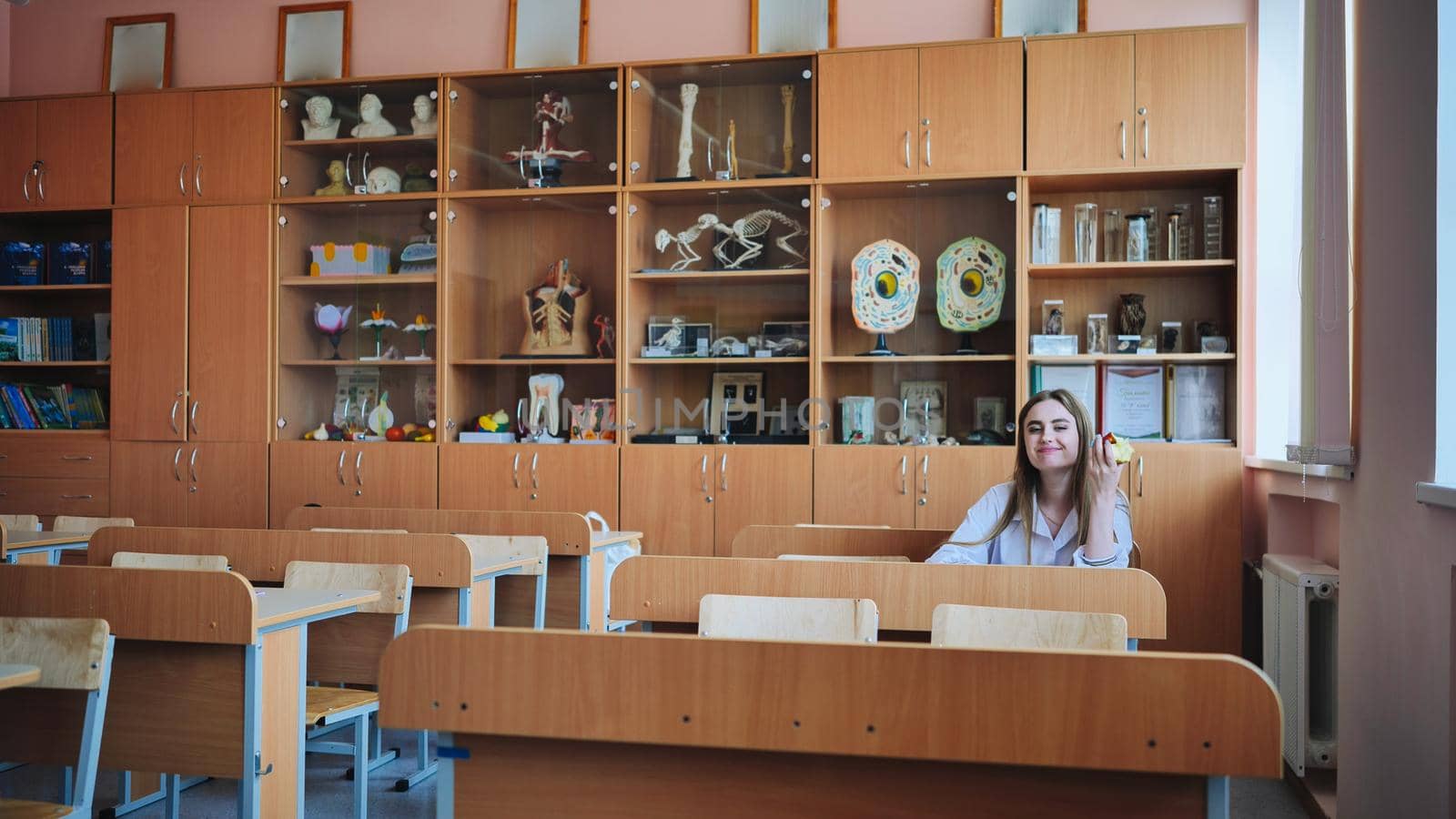 A girl eats an apple in an empty classroom during recess