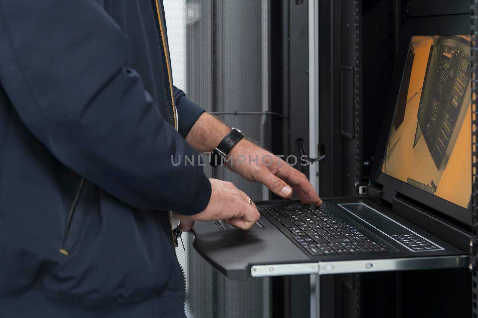 Close up on Data Center Engineer hands Using keyboard on a supercomputer Server Room Specialist Facility with Male System Administrator Working with Data Protection Network for Cyber Security. by dotshock