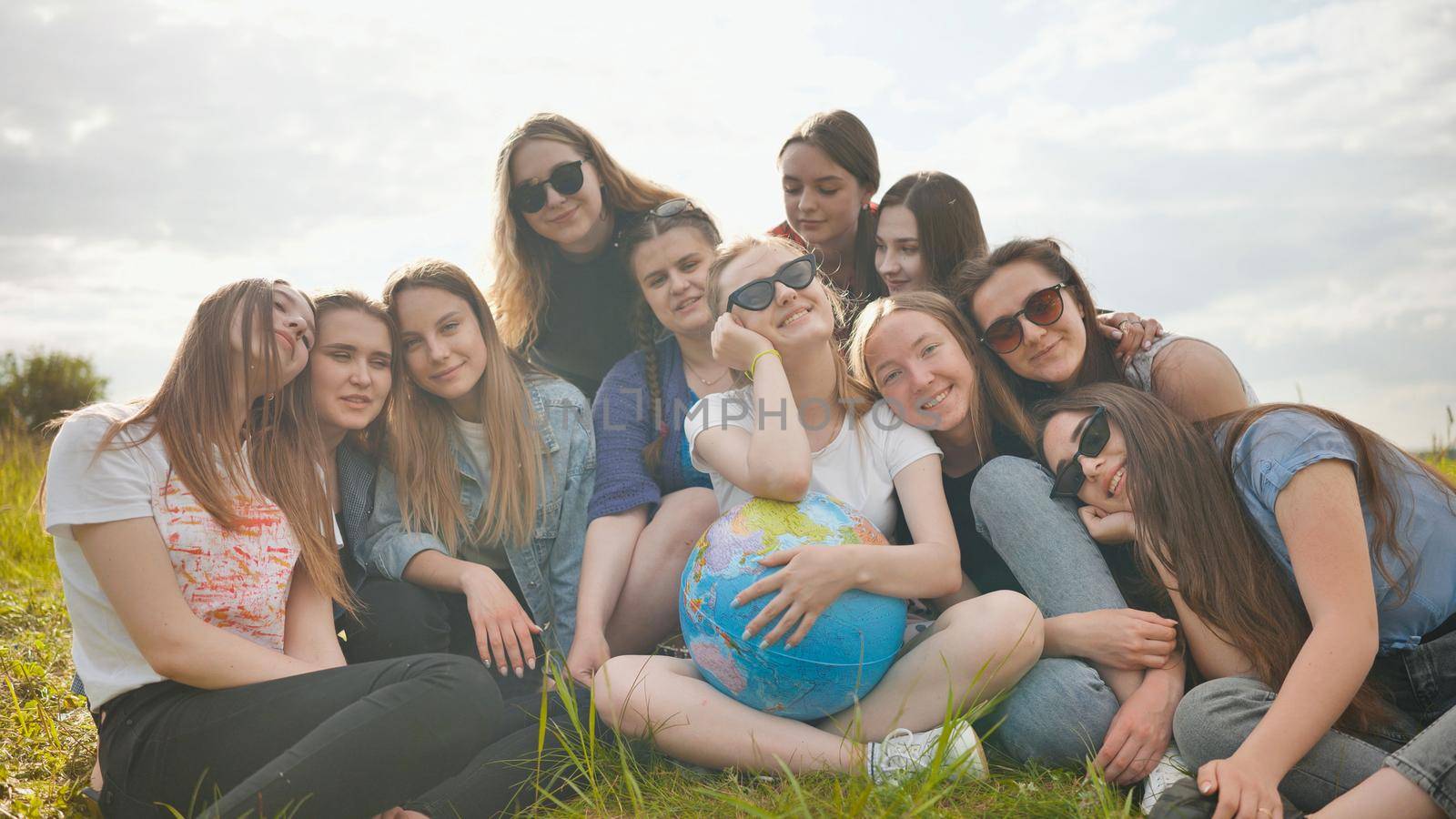 A group of cheerful girls is exploring the globe of the world in the meadow. by DovidPro