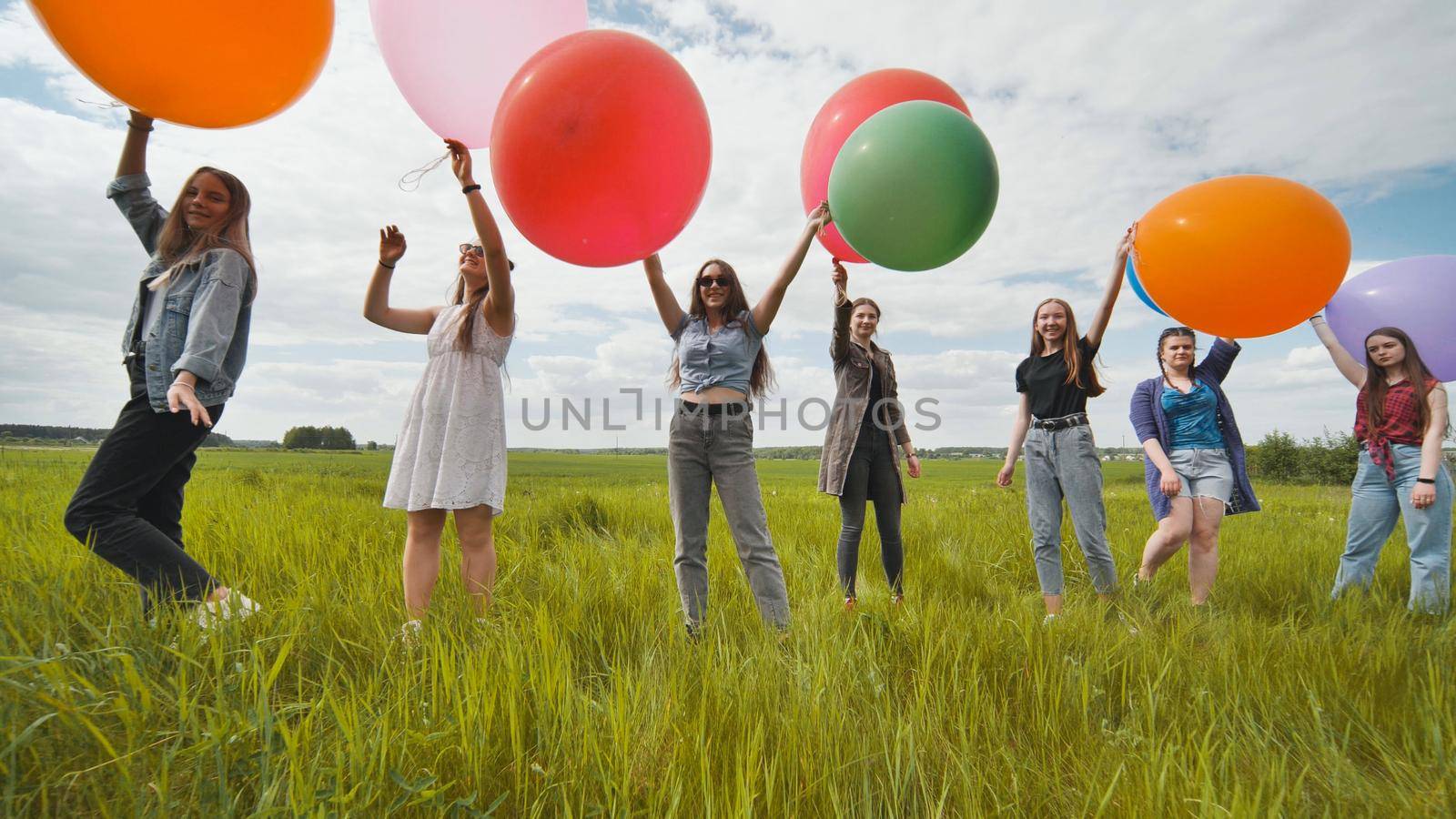 Girls friends are walking across the field with large balloons and colorful balloons. by DovidPro