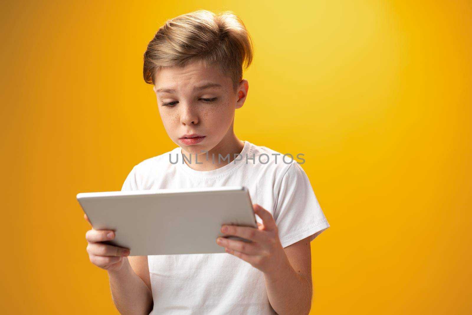 Little boy playing with digital tablet against yellow background, close up