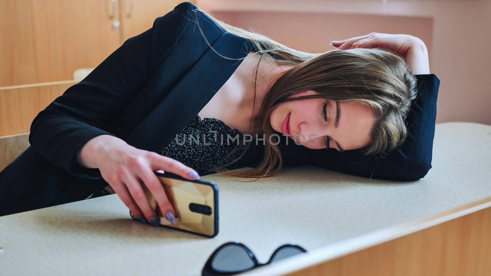 A tired student lying on her desk looks at her smartphone and then smiles