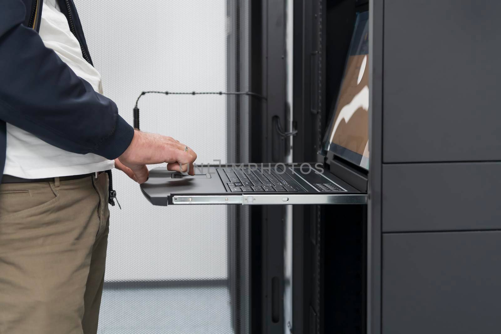 Close up on Data Center Engineer hands Using keyboard on a supercomputer Server Room Specialist Facility with Male System Administrator Working with Data Protection Network for Cyber Security. by dotshock