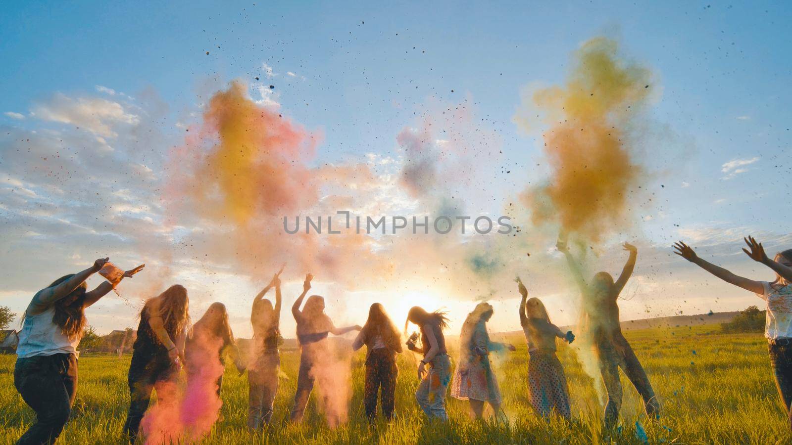 Cheerful girls toss up multi-colored powder at a beautiful sunset