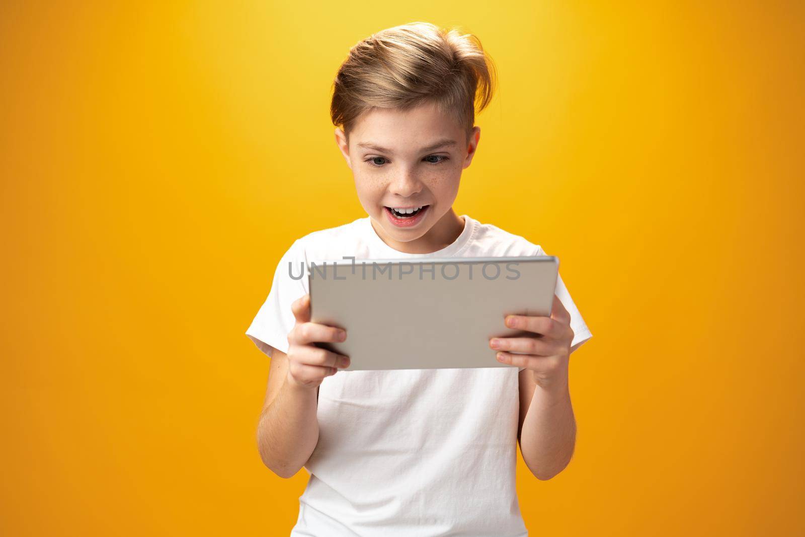 Little boy playing with digital tablet against yellow background, close up