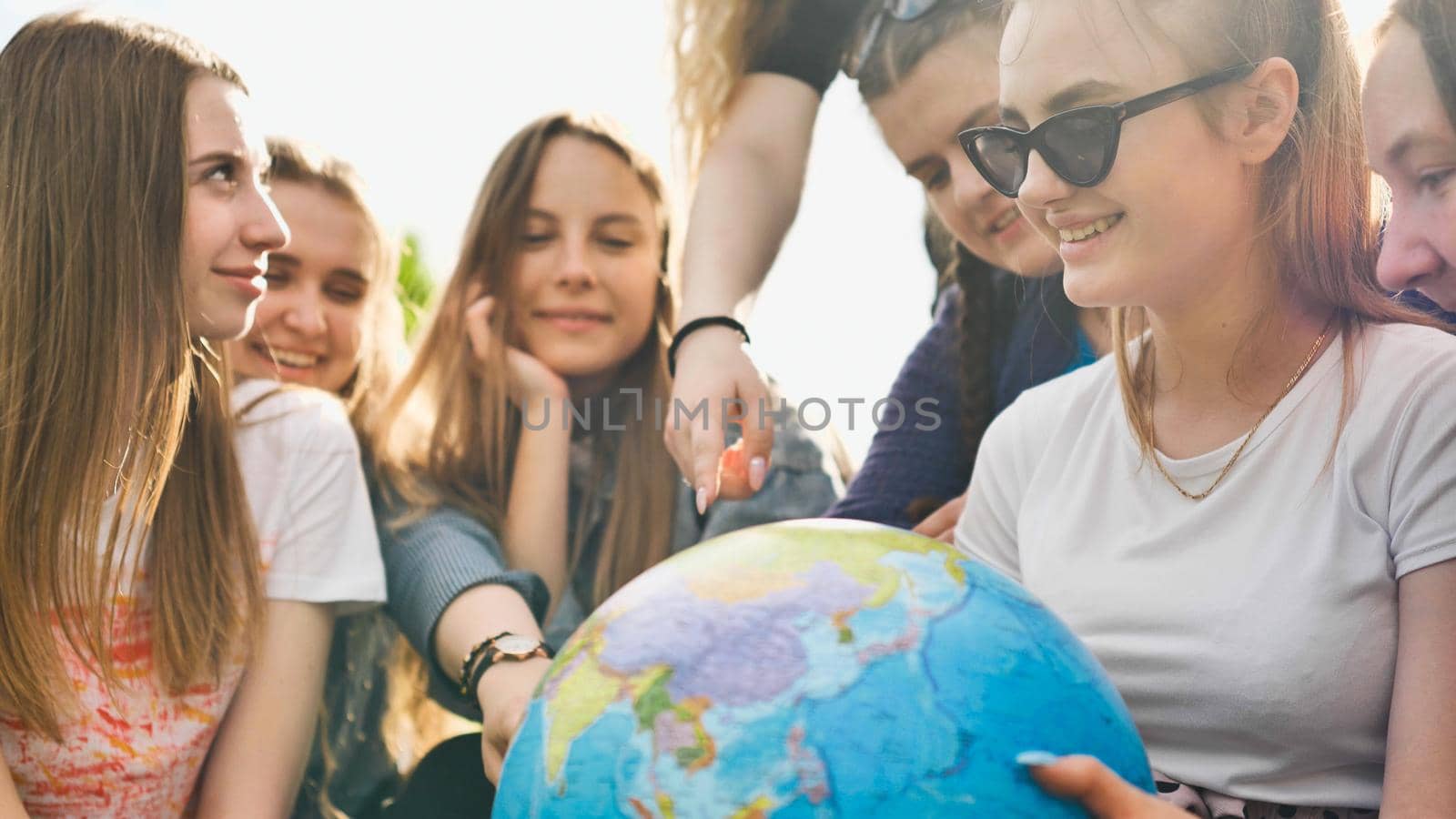 A group of cheerful girls is exploring the globe of the world in the meadow