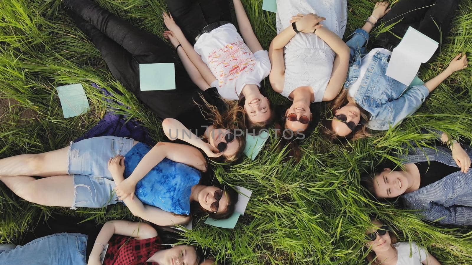 Girls students lie on the grass in a city park with notebooks. by DovidPro