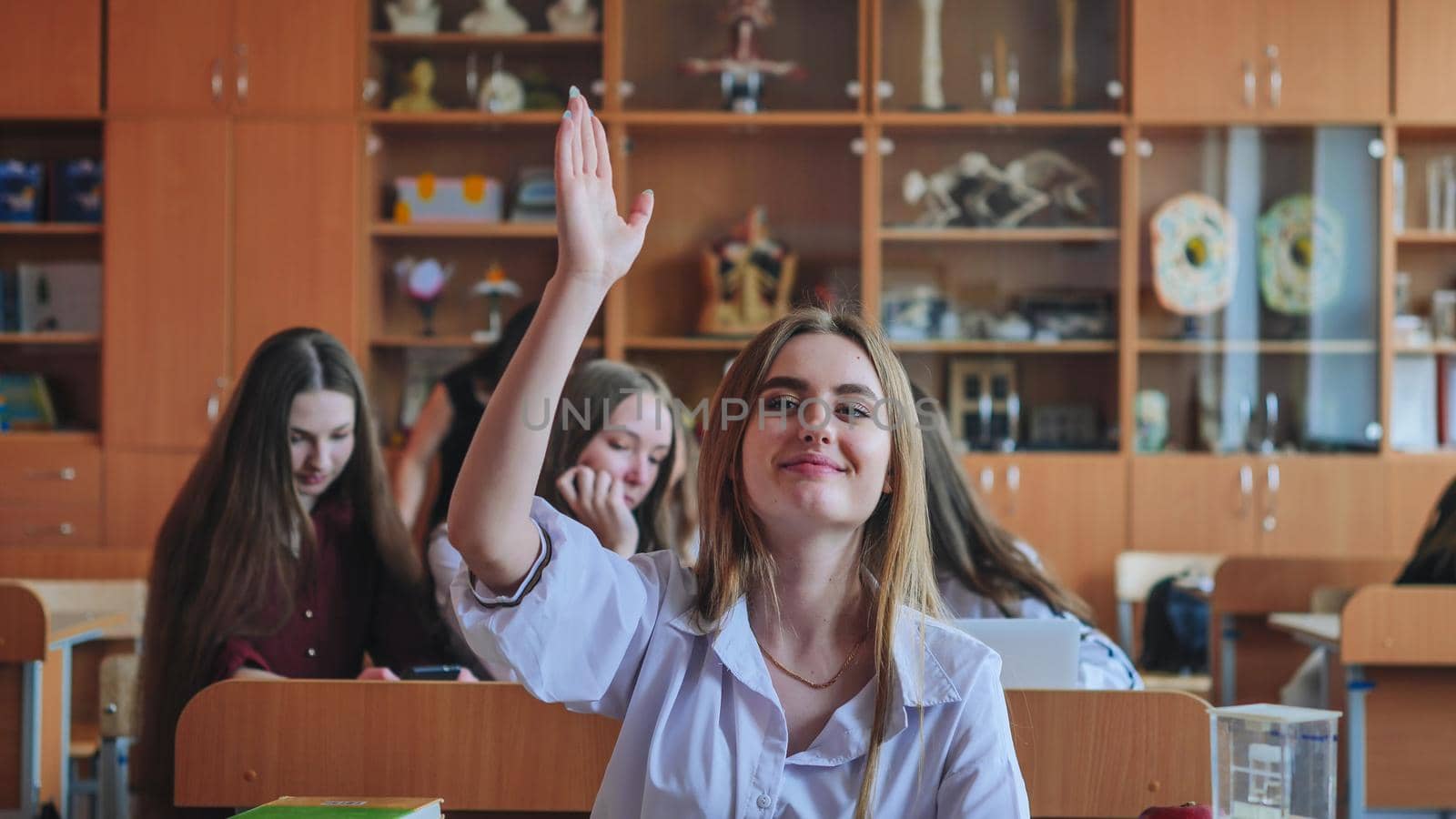 A girl student sitting at a desk raises her hand in the class