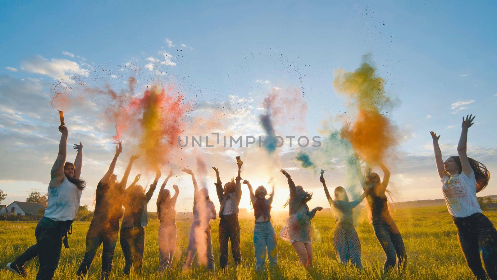 Cheerful girls toss up multi-colored powder at a beautiful sunset