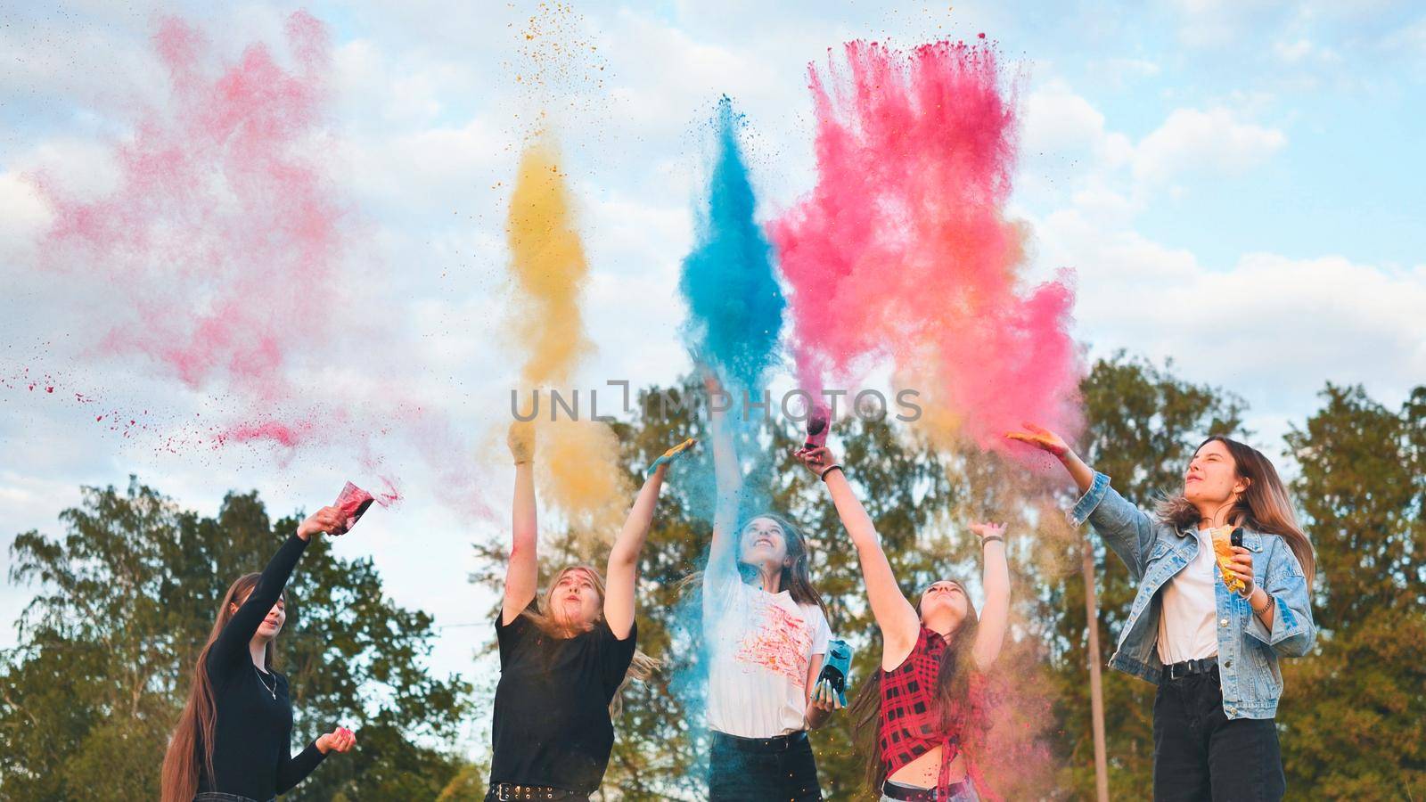 Cheerful girls toss up multi-colored powder. Holi holiday