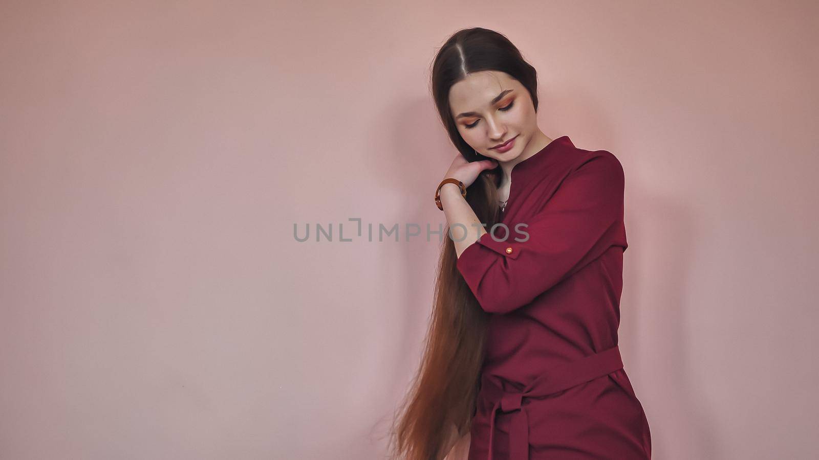 Long-haired girl combs her hair on a pink background