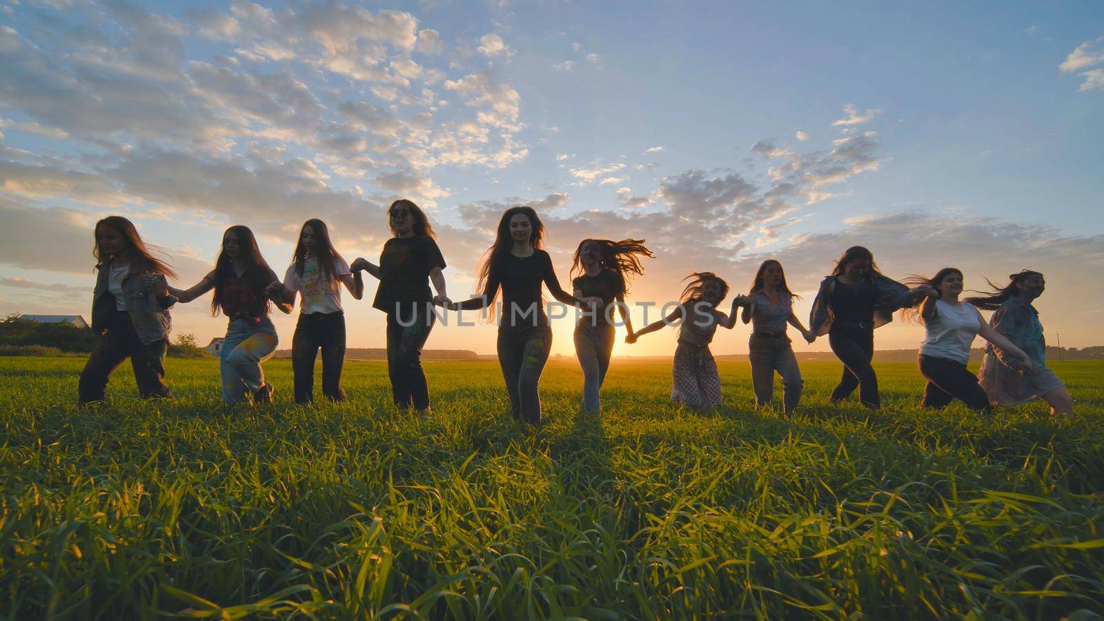 A group of girls walk towards the sun at sunset holding hands. by DovidPro