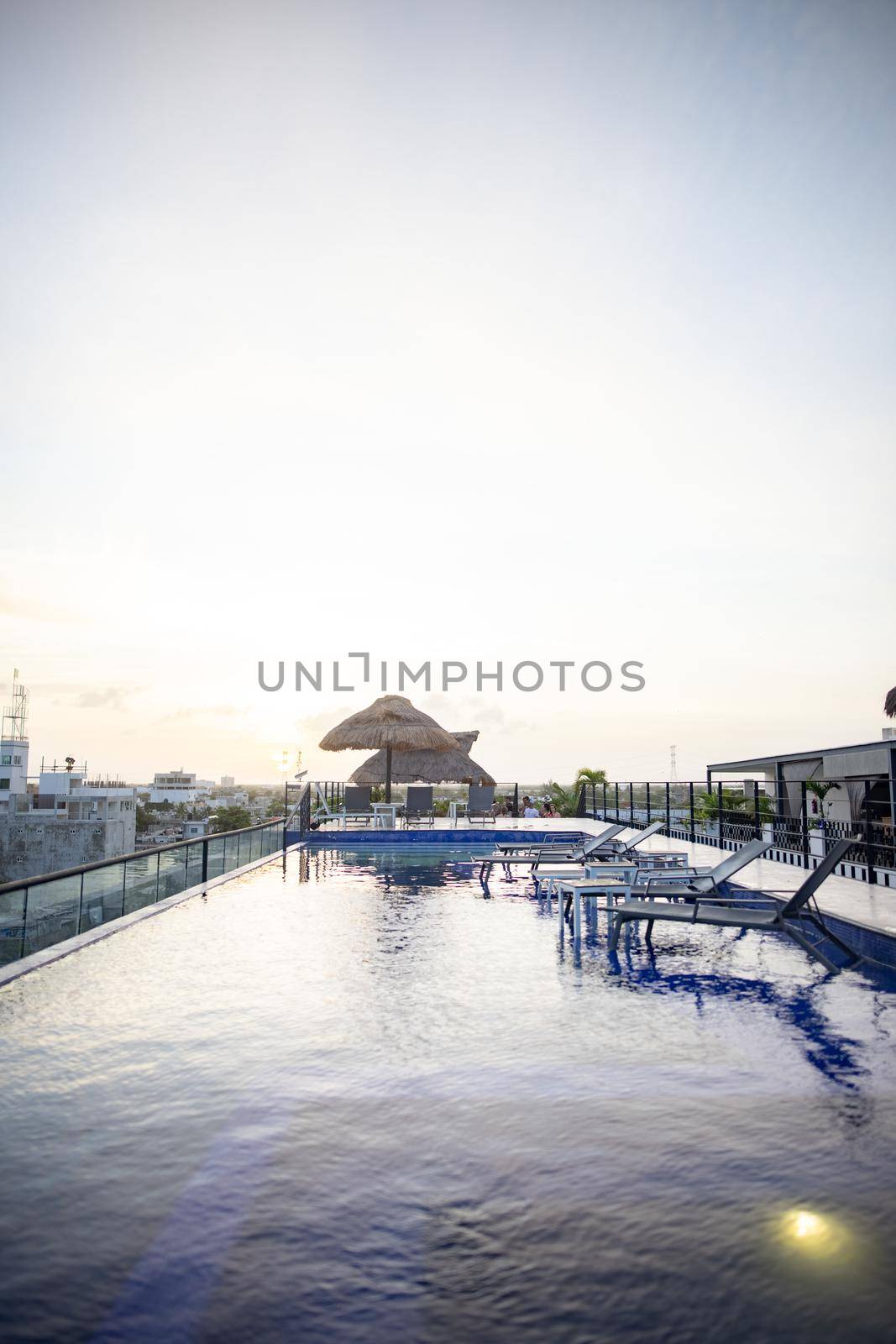 Beautiful view of umbrellas and shallow pool with beach beds in hotel under bright sky. Peaceful view of white skyline above tropical resort rooftop. Holidays and landscapes