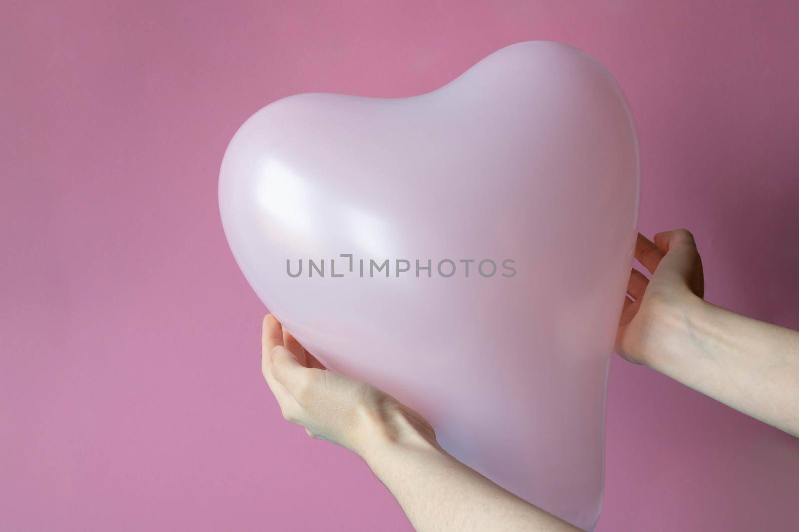 Women's hands hold a pink ball in the shape of a heart, highlighted on a pink background.