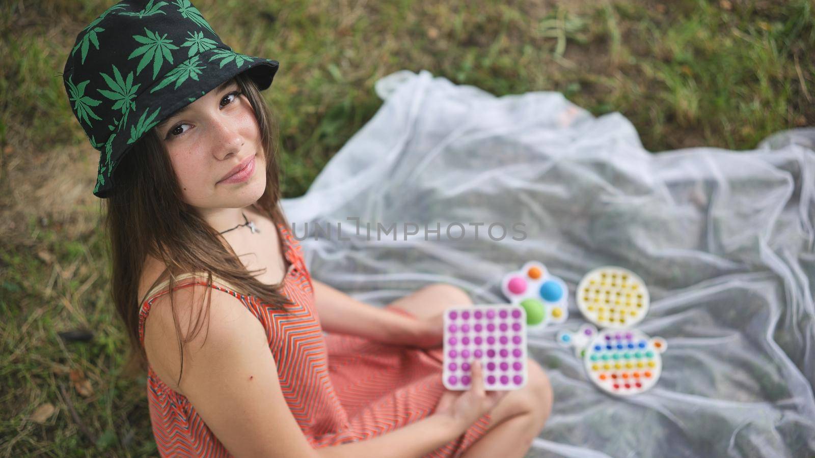 Teenage girl playing with a toy popit on the meadow in the park