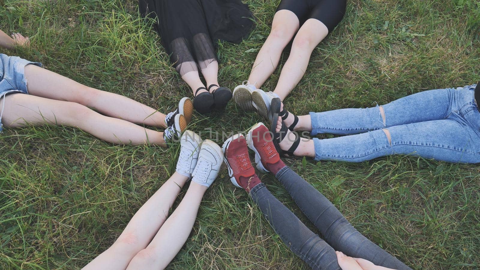 Friends are sitting on the grass with their legs joined in a circle