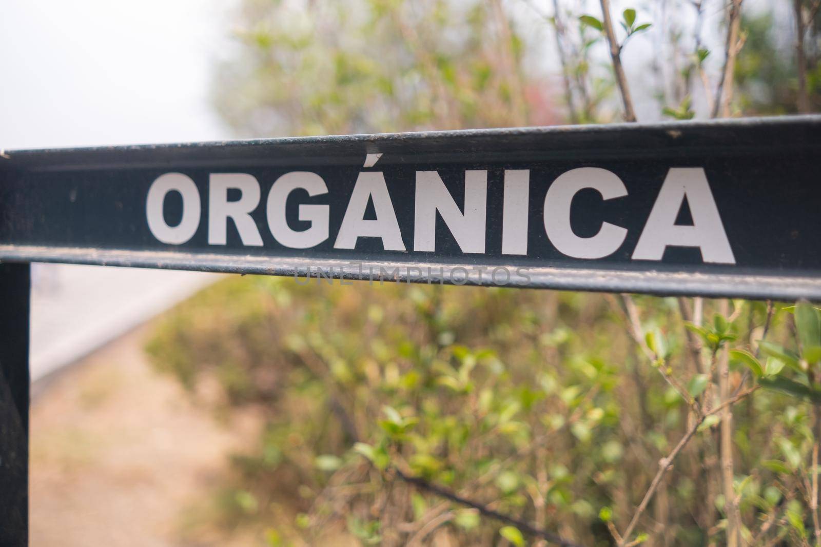 Close-up of Spanish sign for organic trash in park from Mexico City. White capital letters in black metal bar with blurry plants as background. Environment and outdoors