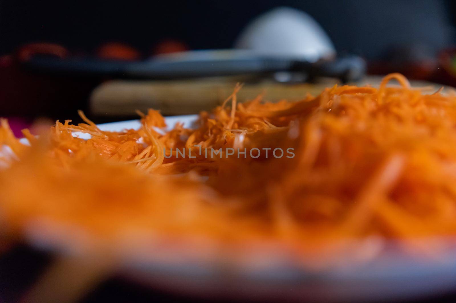 Extreme close-up of small pile of grated carrot on white plate with blurry background. Tasty and fresh shredded carrot above porcelain plate. Vegetables and healthy food preparation