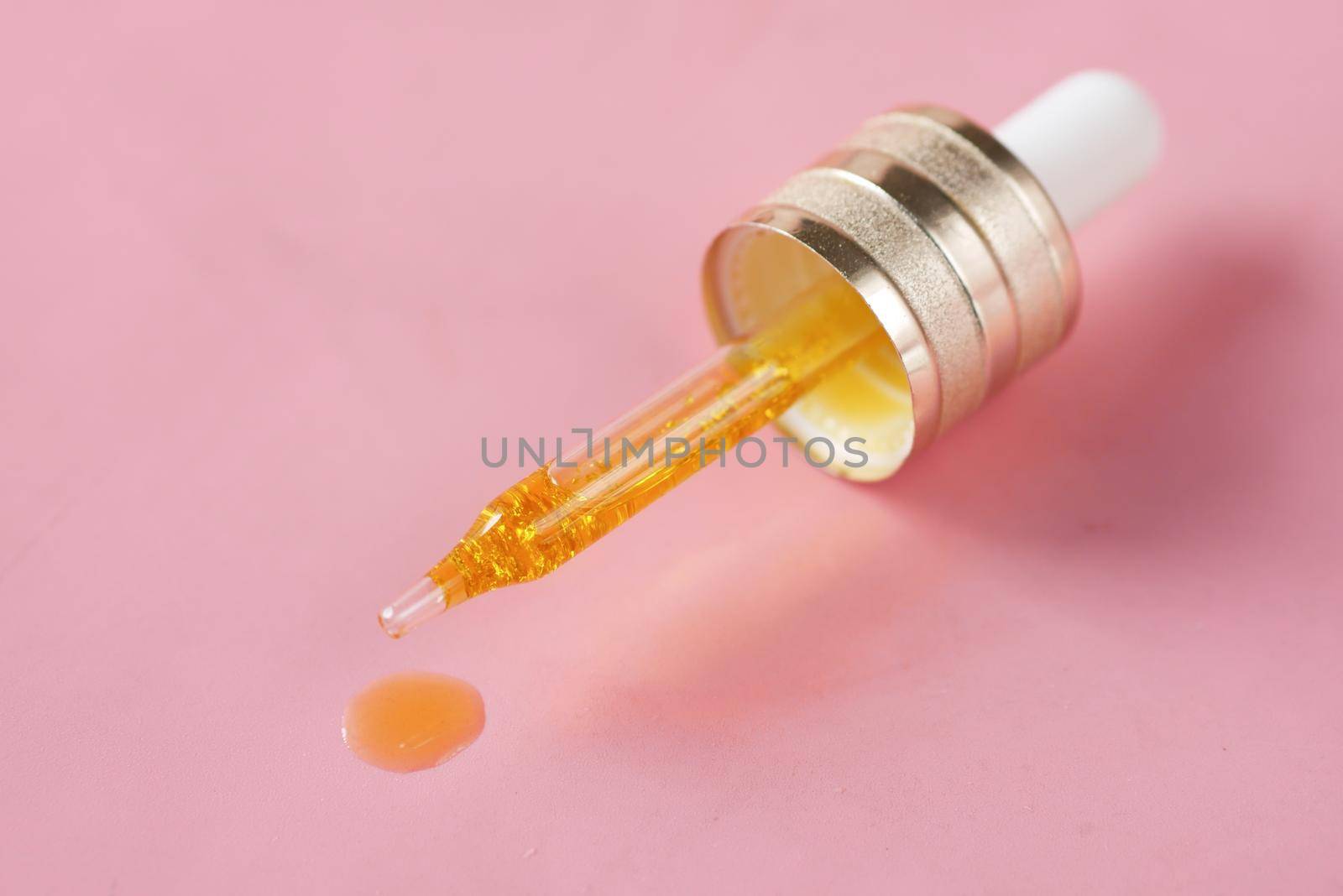 Drop falls from a pipette on pink background .