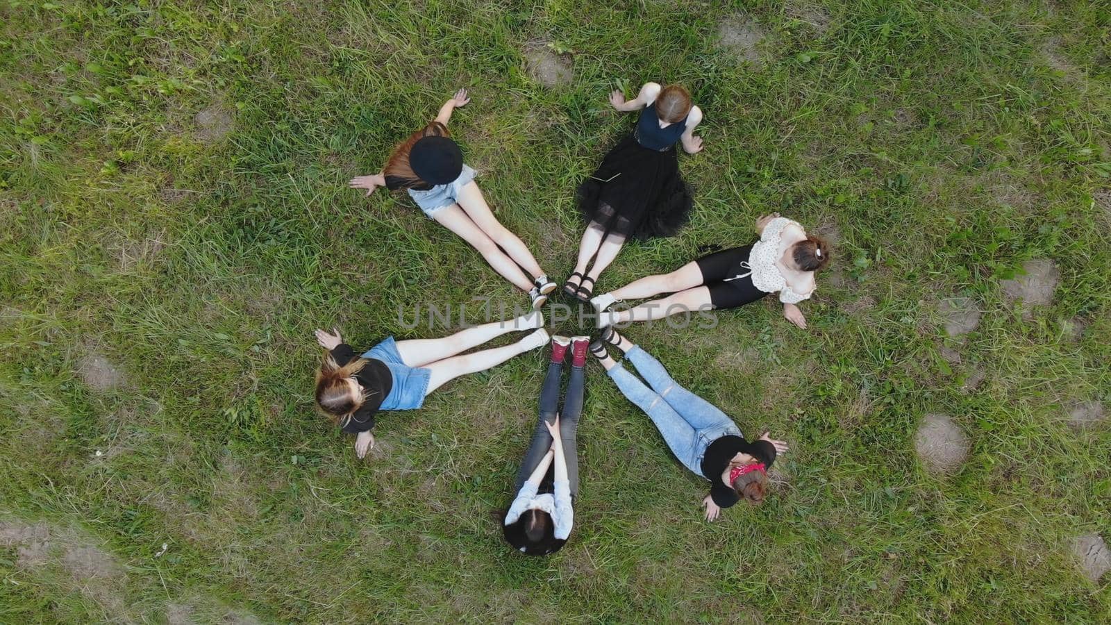 Friends are sitting on the grass with their legs joined in a circle